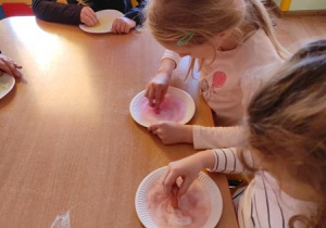Dziewczynki piszą literki na zabarwionej soli.